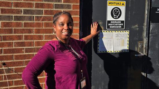 Portrait of Kim Haley outside of a building, posing next to a sign on a door that reads 